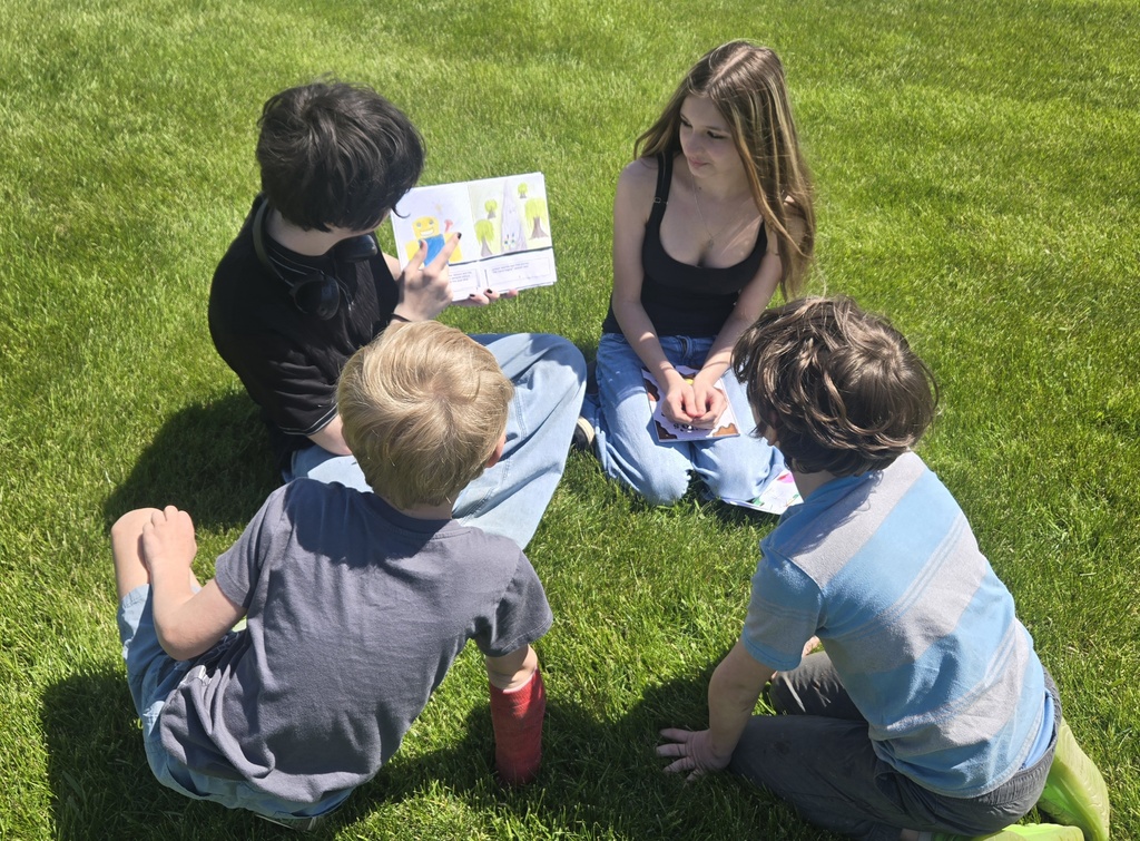 2 middle school students reading in the grass with 2 1st grade students