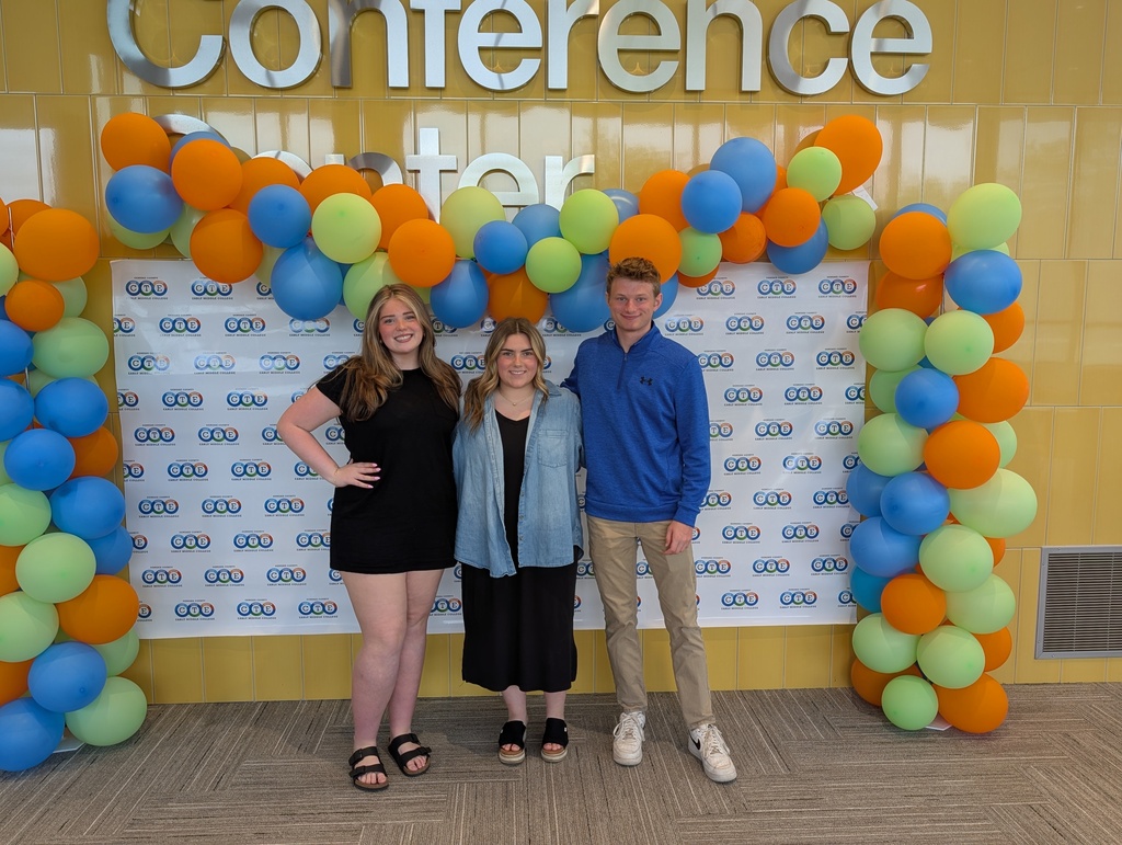 3 high school students posing in front of a colorful backdrop with balloons