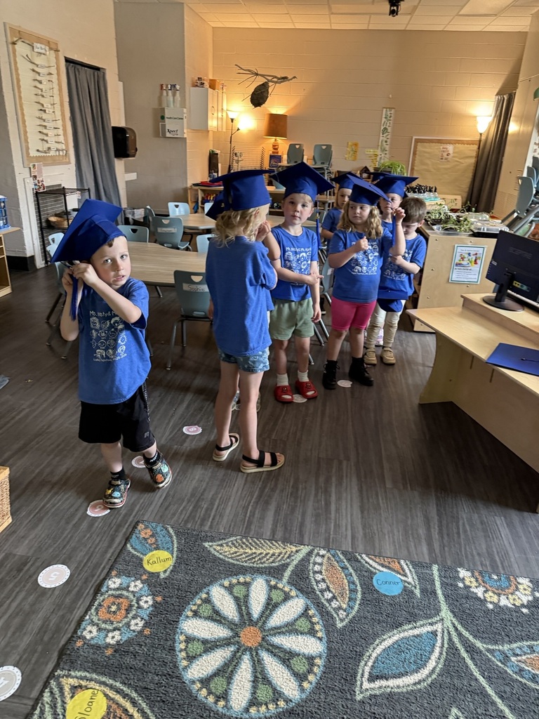 children in a classroom wearing blue graduation caps