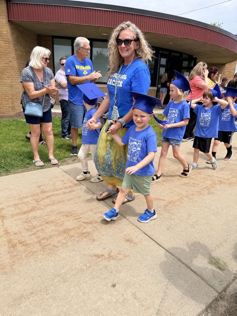 children walking in a line with a teacher and wearing blue graduation caps