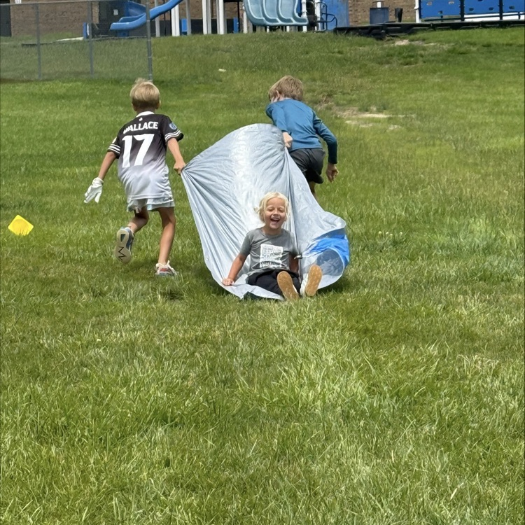 kids pulling another kid around in the grass on a tarp