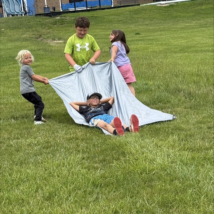 kids pulling another kid around in the grass on a tarp