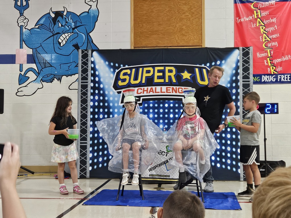 4 children posing in front of a backdrop that says Super U Challenge with 3 of them wearing plastic capes