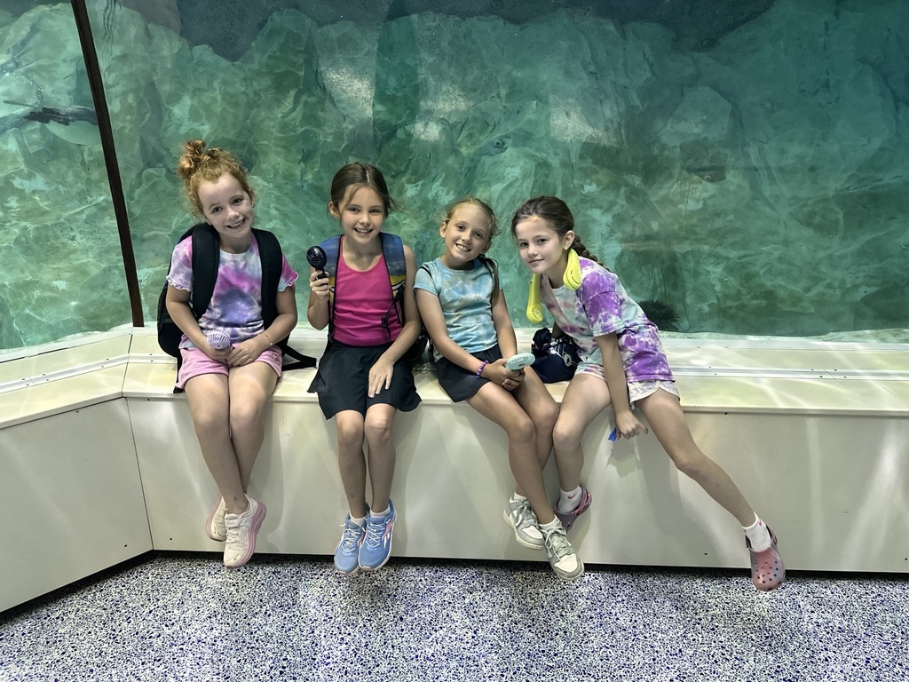 4 girls posing in front of a big aquarium