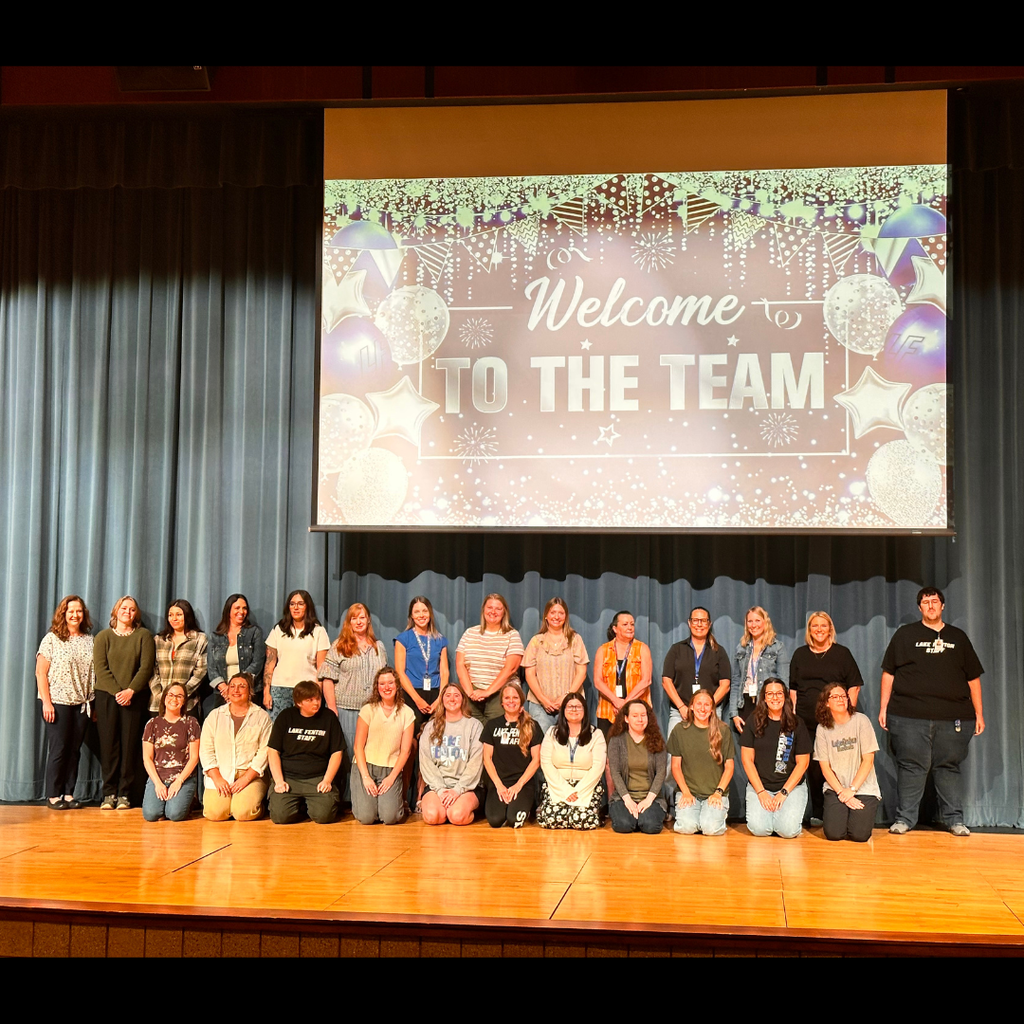 large group of people standing on a stage under a welcome to the team banner