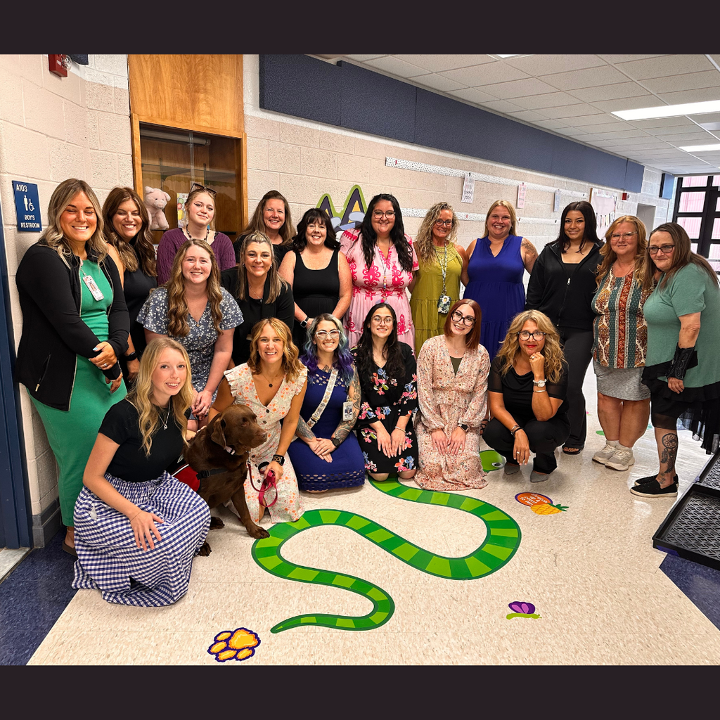 large group of women and a chocolate lab posing in a preschool hallway