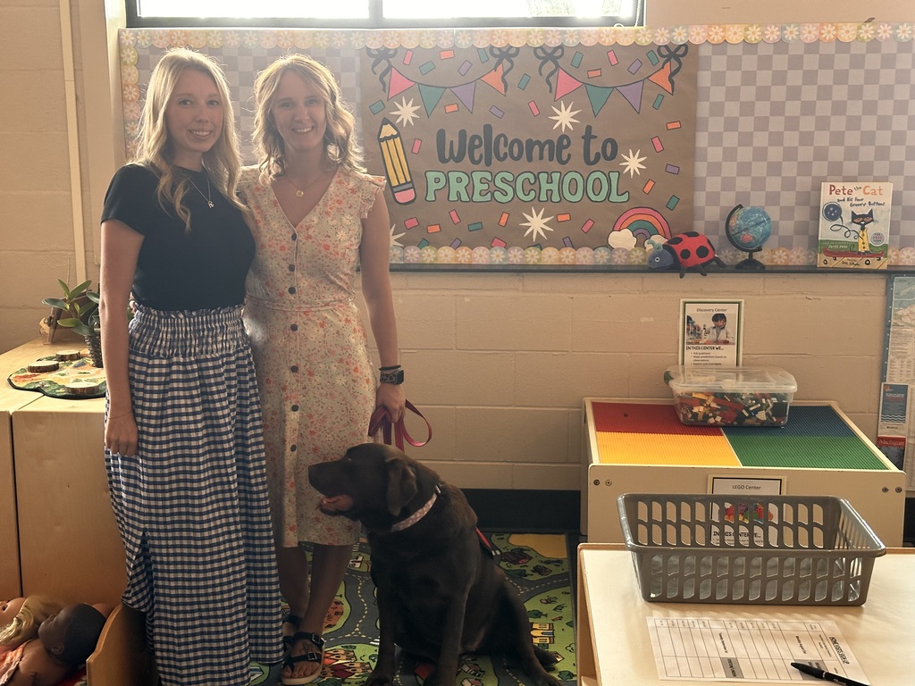 2 women and a chocolate lab posing in a preschool classroom