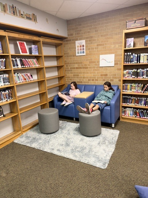2 girls sitting on a blue couch reading in a library