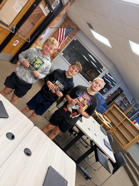 3 boys holding up books in a library