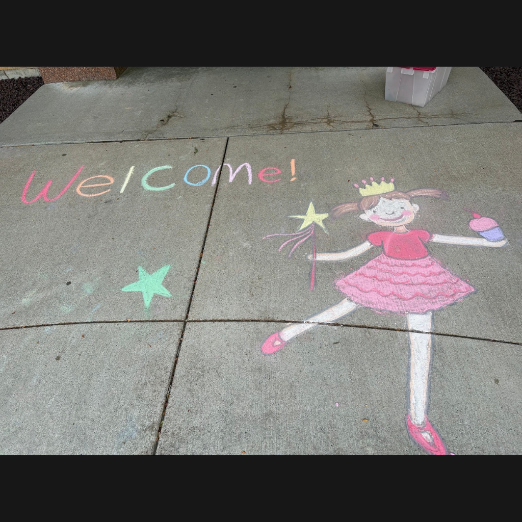 chalk drawing on sidewalk of the word Welcome and a girl dressed like a ballerina