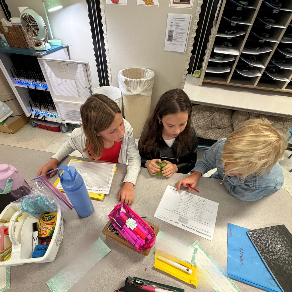 3 kids sitting at a desk in a classroom doing homework