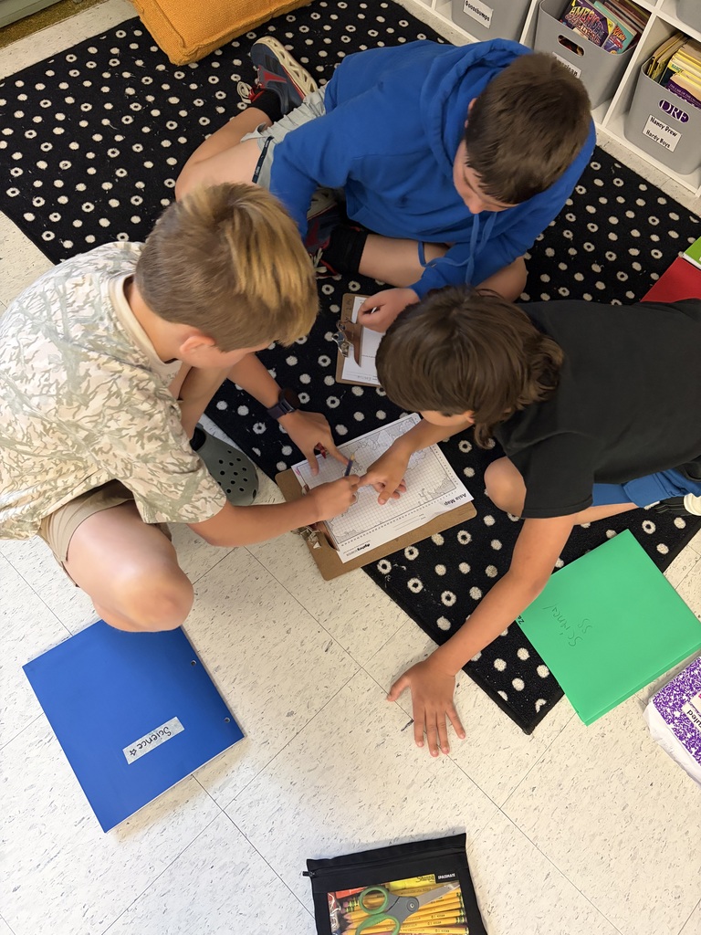 3 kids sitting in a circle on a classroom floor doing homework