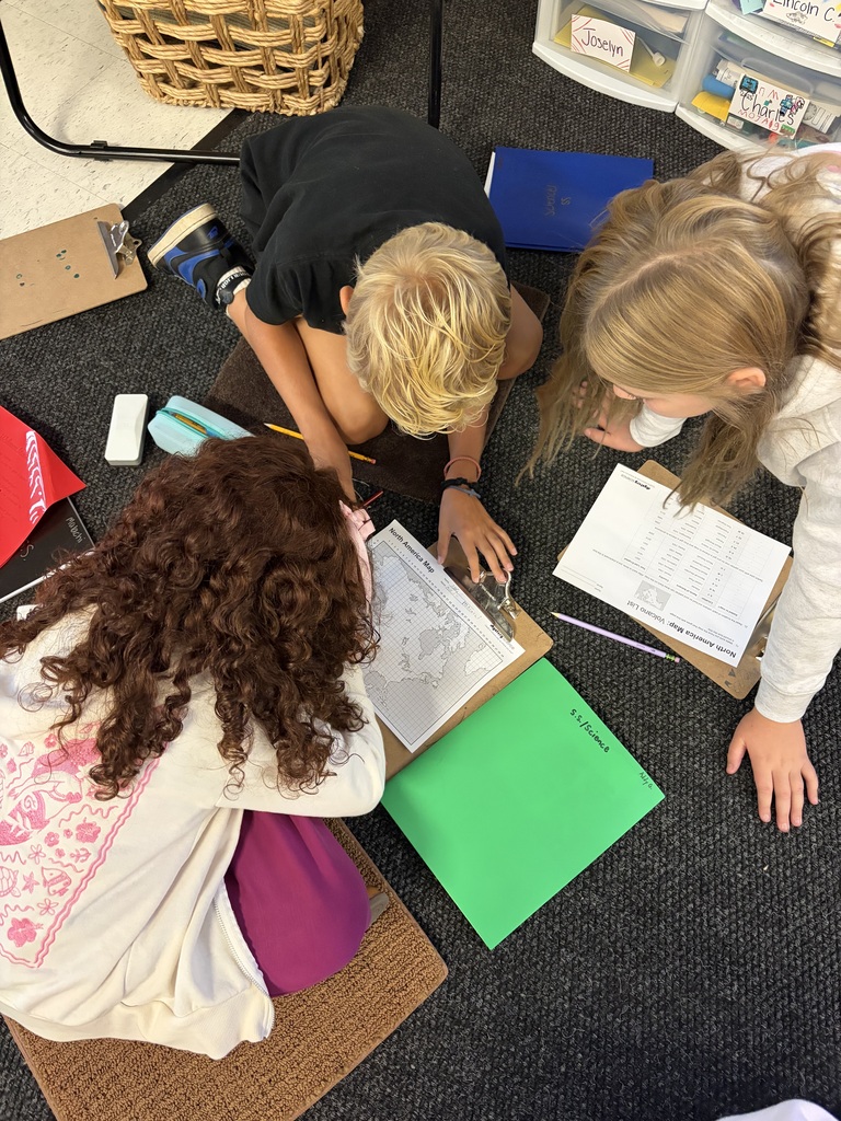 3 kids sitting in a circle on a classroom floor doing homework