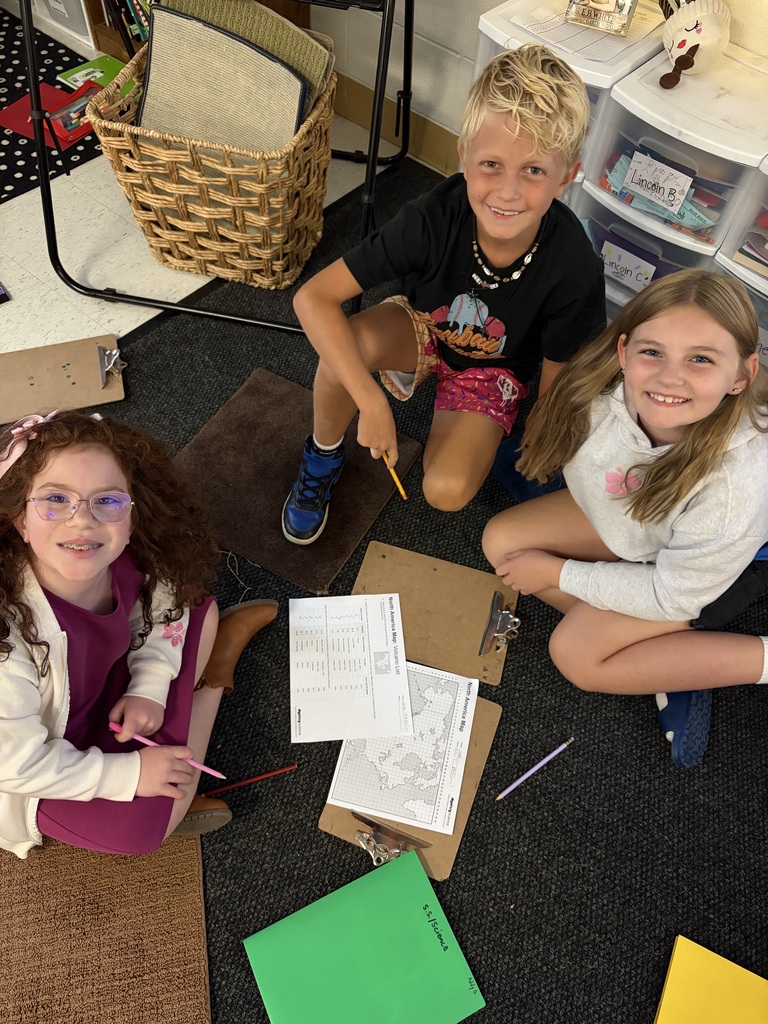 3 kids sitting in a circle on a classroom floor doing homework