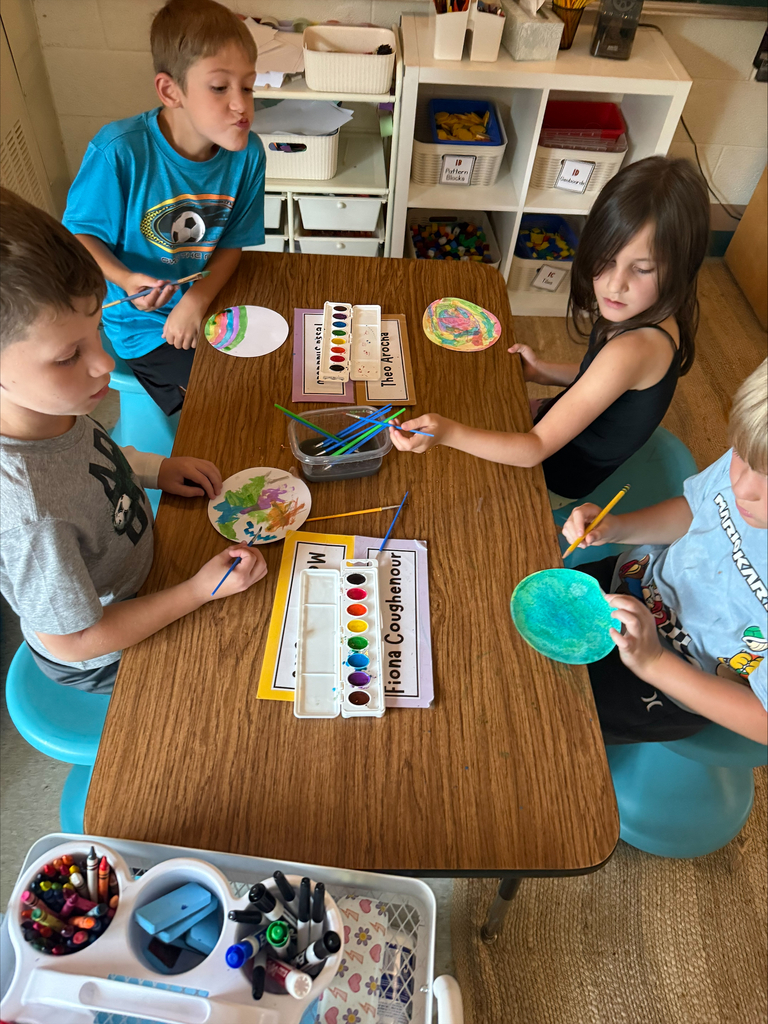 group of students sitting at a table in a classroom painting with watercolors