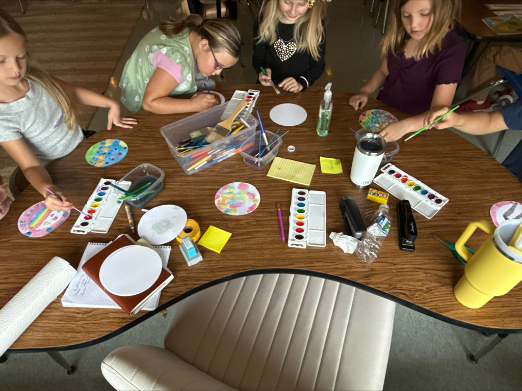 group of students sitting at a table ion a classroom painting with watercolors