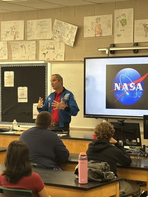 man in blue jacket speaking in a classroom