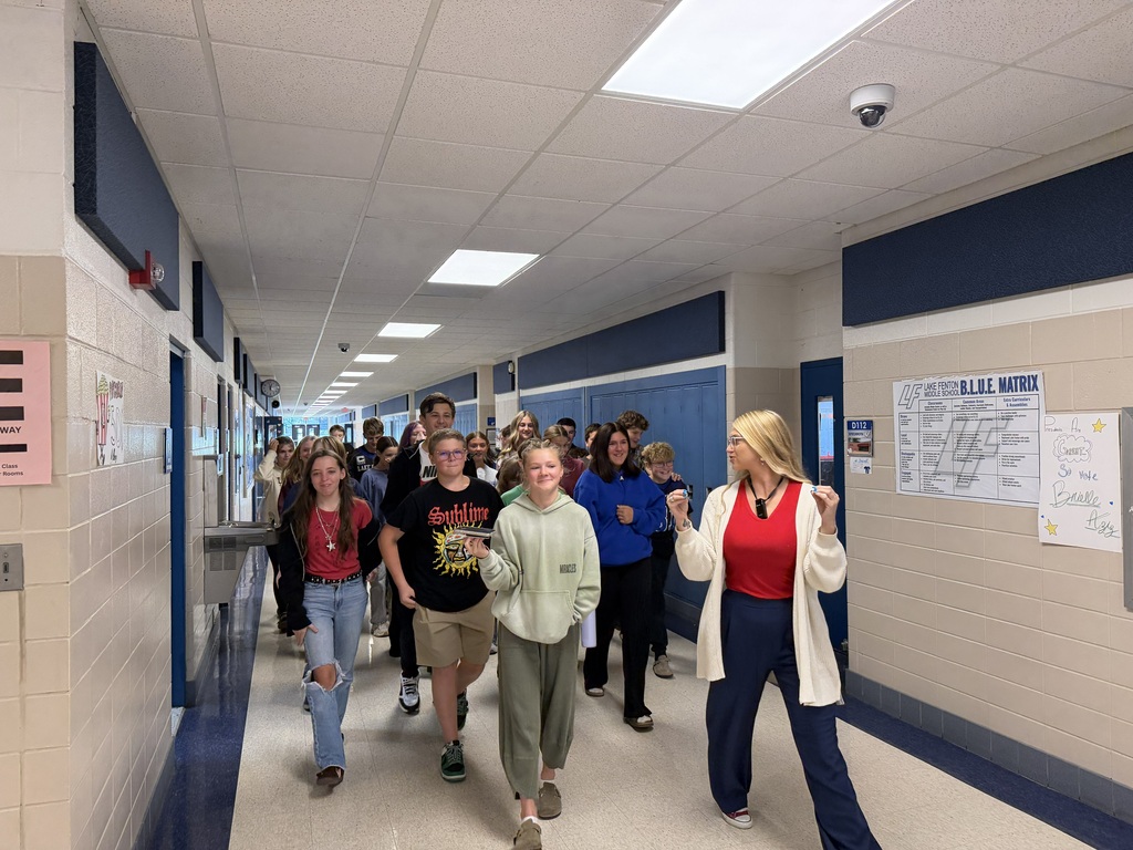 teacher leading a group of students down a school hallway