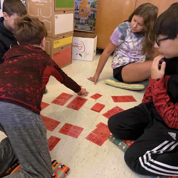 4 children sitting on a classroom floor working with red cards
