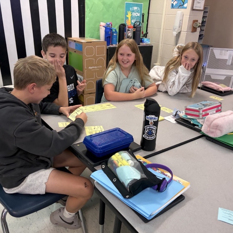 4 children sitting around desks working with yellow cards