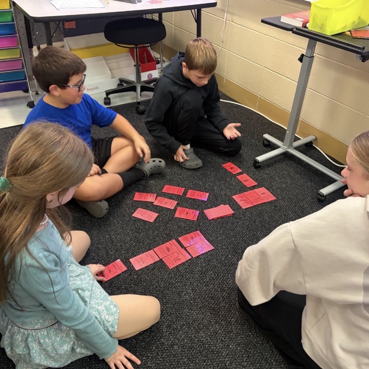 4 children sitting on a classroom floor working with red cards