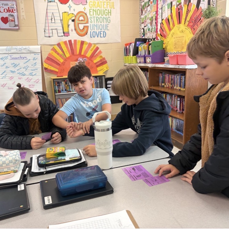 4 children sitting around a desk working with purple cards