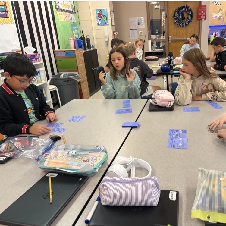 3 children sitting around a desk working with blue cards