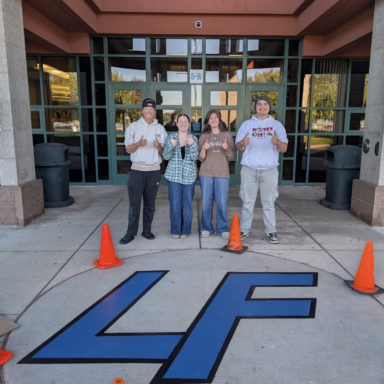 4 students posing in front of a blue LF logo painted on cement 