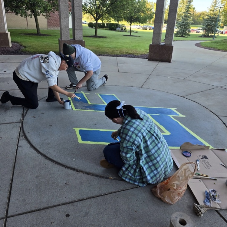 3 students painting a blue LF logo on cement