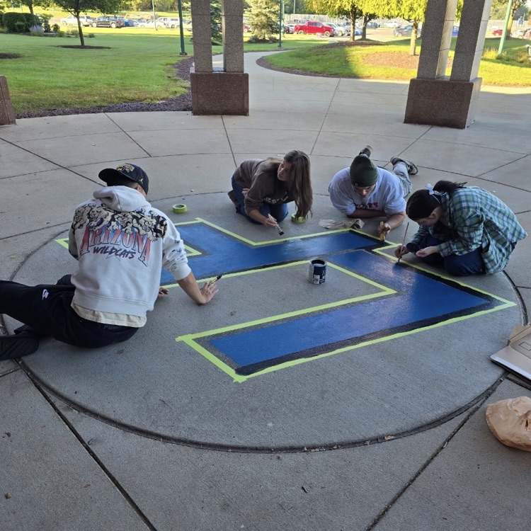 4 students painting a blue LF logo on cement