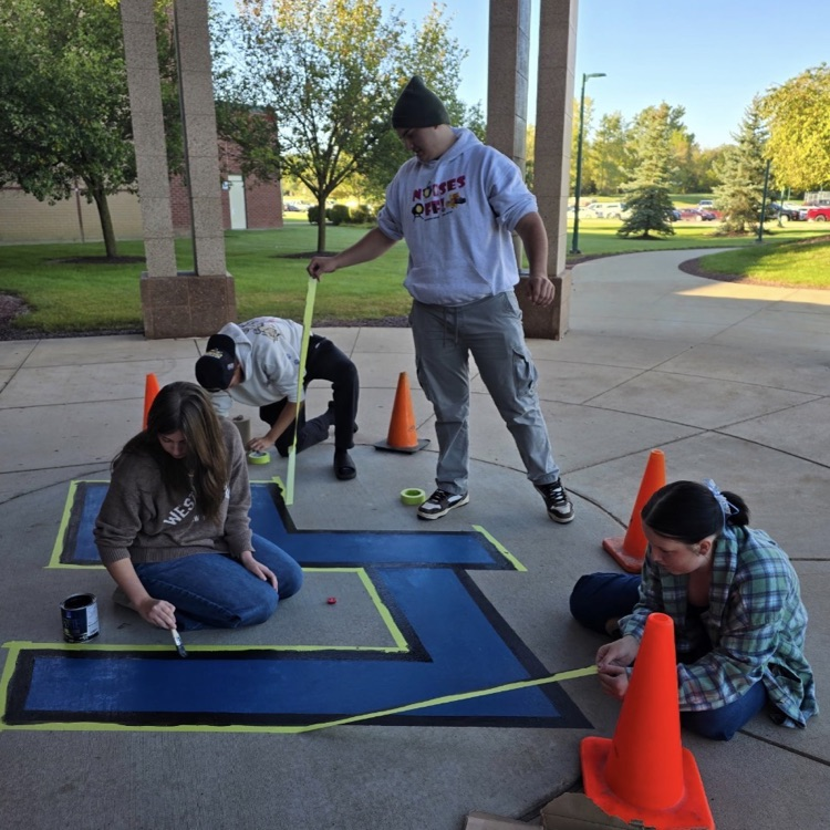 4 students painting a blue LF logo on cement