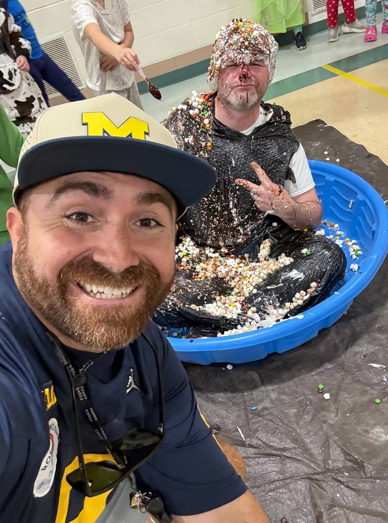 man smiling next to another man that is sitting in a small blue pool covered in ice cream toppings