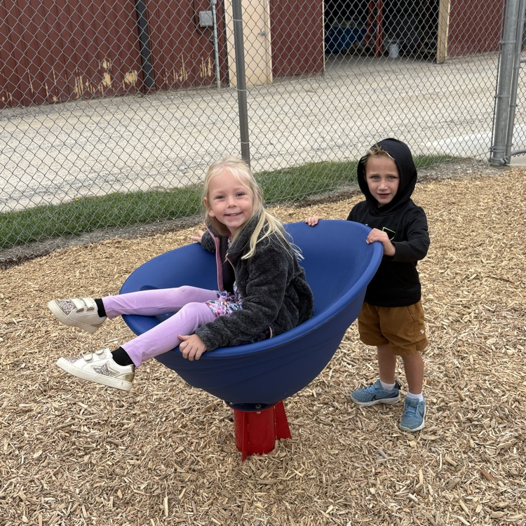 boy spinning a girl in a blue spinner on a playground