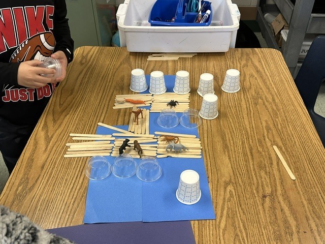 students making bridges out of cups and Popsicle sticks for small, plastic animals