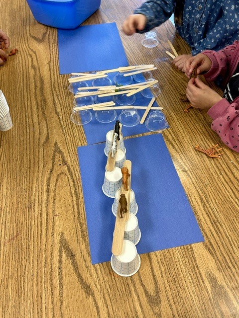 students making bridges out of cups and Popsicle sticks for small, plastic animals