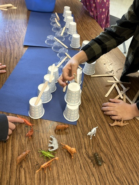 students making bridges out of cups and Popsicle sticks for small, plastic animals