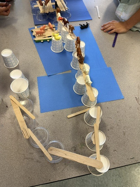 students making bridges out of cups and Popsicle sticks for small, plastic animals