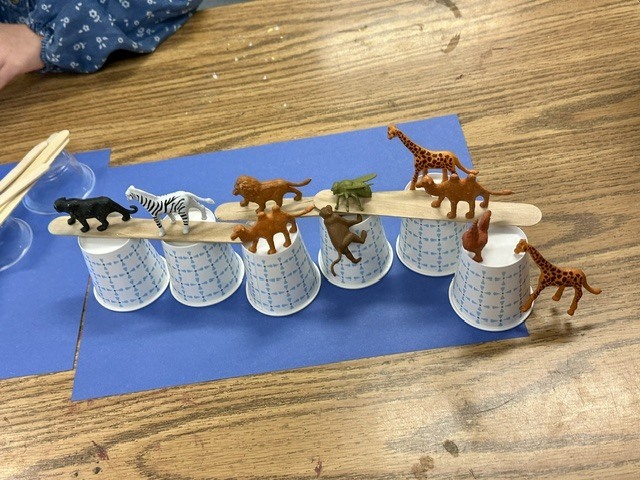 students making bridges out of cups and Popsicle sticks for small, plastic animals