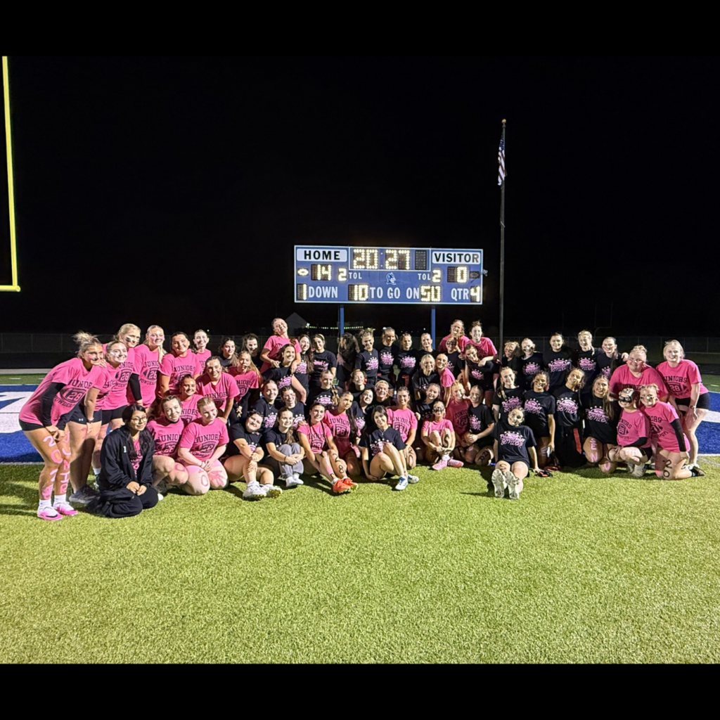 large group of girls posing on a football field in pink shirts