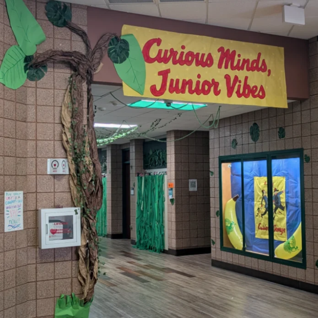a decorated school hallway with a large banner that says Curious Minds, Junior Vibes