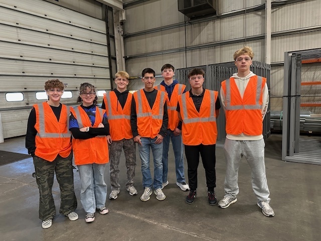 group of students posing in a warehouse wearing orange vests