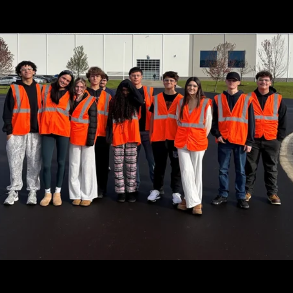 group of students posing outside a warehouse wearing orange vests
