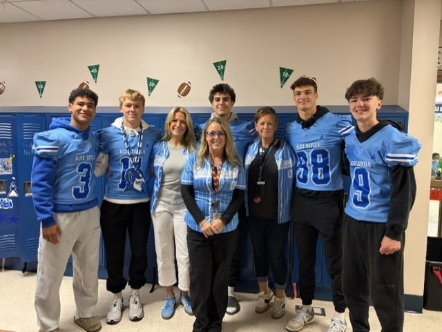 football players in blue jerseys posing with a teacher