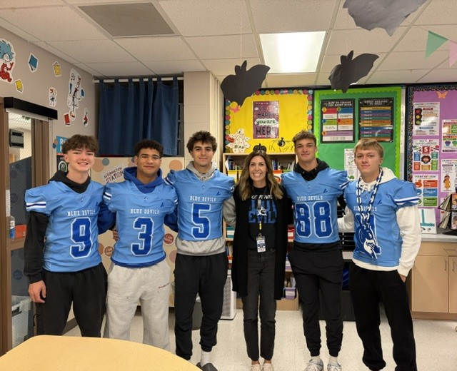 football players in blue jerseys posing with a teacher