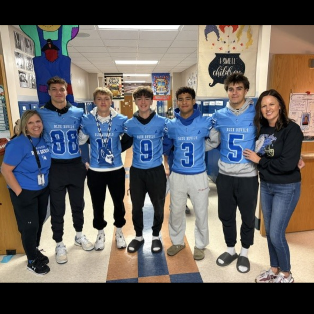 football players in blue jerseys posing with a teacher