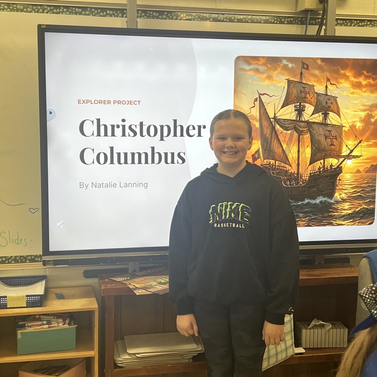 student standing next to a smart board with a presentation about Christopher Columbus