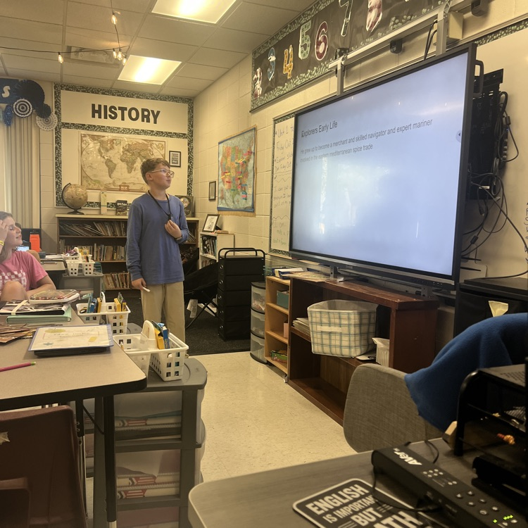 student standing in front of a class reading off of a smart board. 
