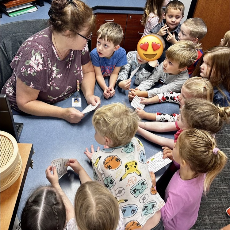 group of preschoolers gathered around a woman sitting at her desk