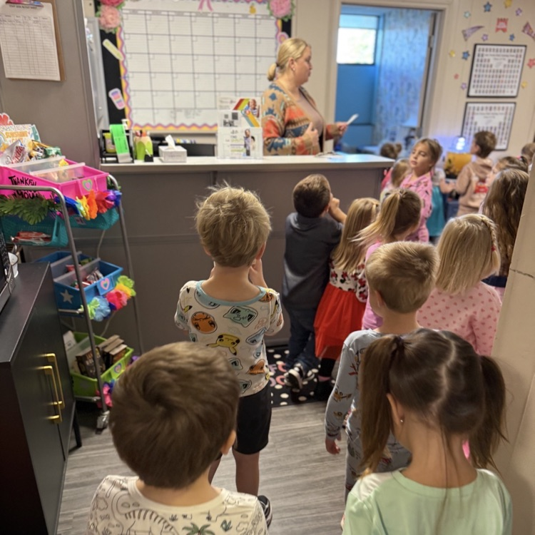 wo man standing behind his desk reading from a small piece of paper to a large group of children