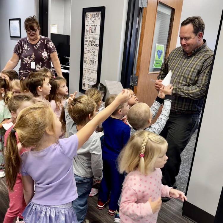 man standing in front of an office reading to a large group of children